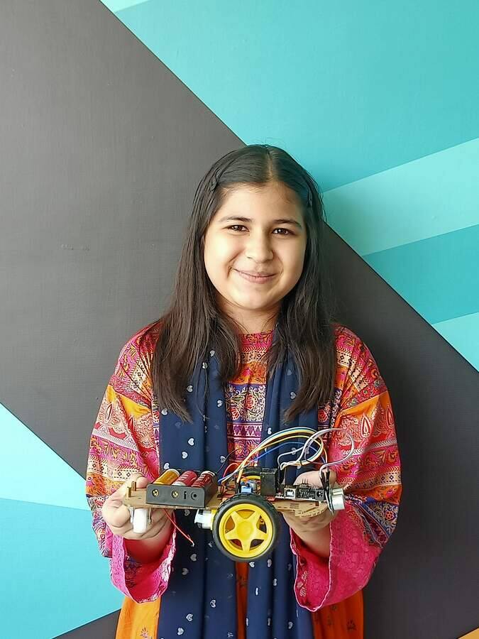 Student proudly holding the obstacle-avoiding robot she built at a STEMForge robotics workshop in Lahore