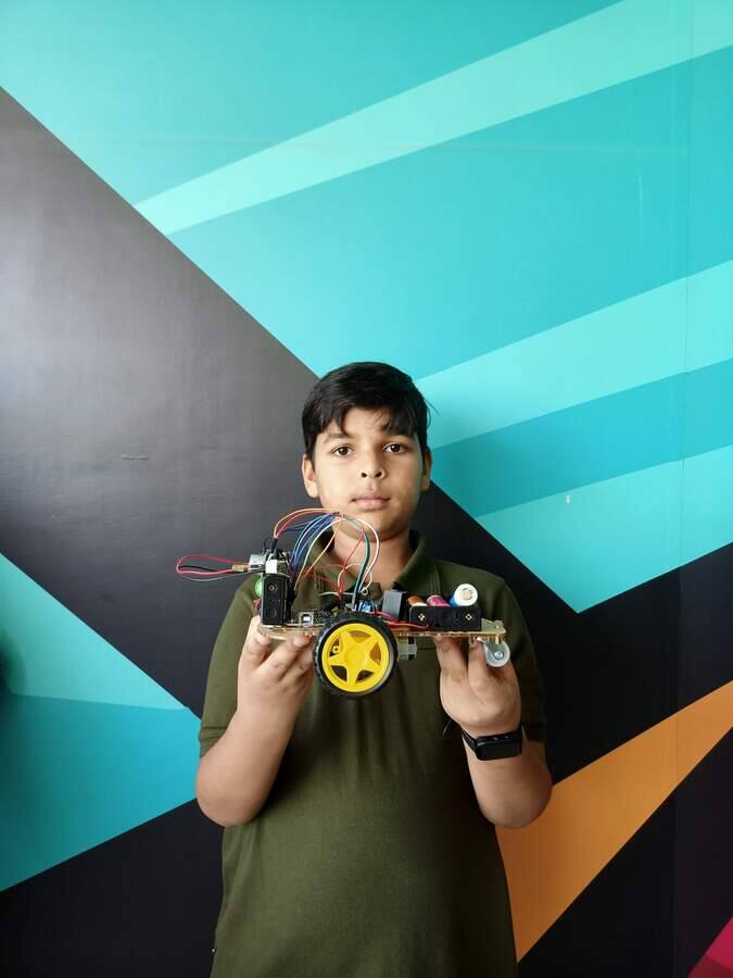 Student holding a completed Arduino robot car built in a STEMForge robotics workshop